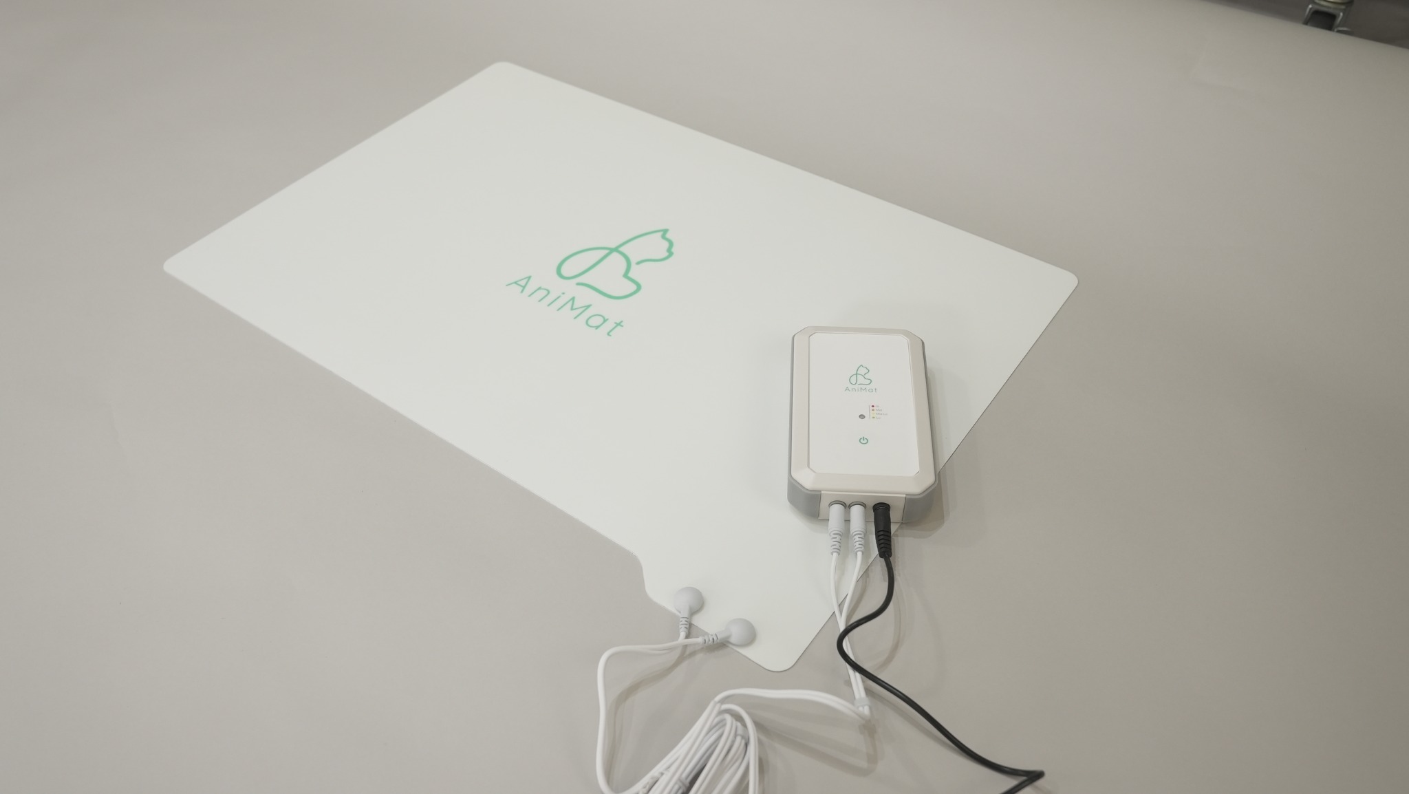 AniMatの商品写真。ミント色のロゴが入った薄い白いマットと、専用コントローラー・接続ケーブル
